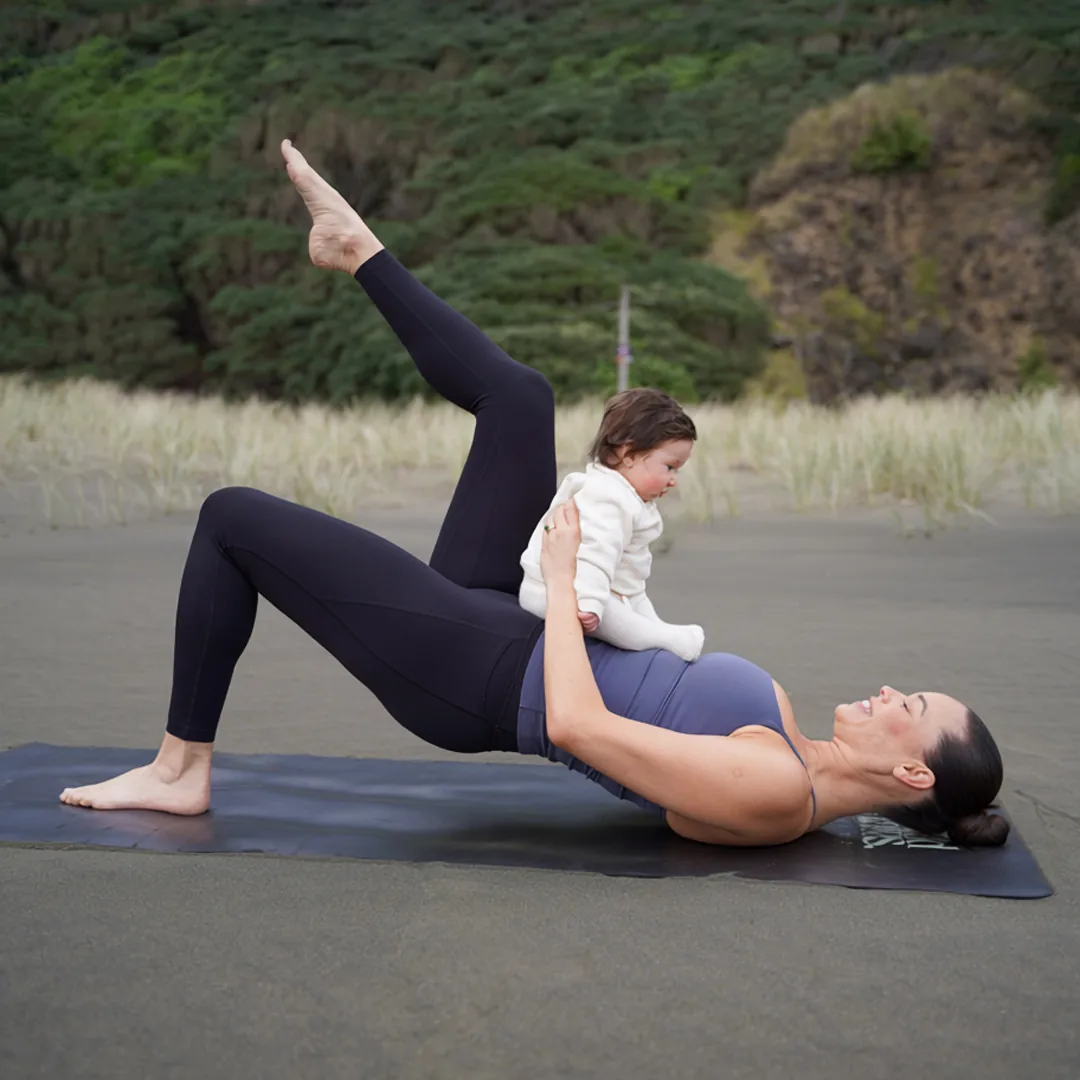 Laura Mohi Ryan doing a postnatal Pilates bridge with her baby on the beach